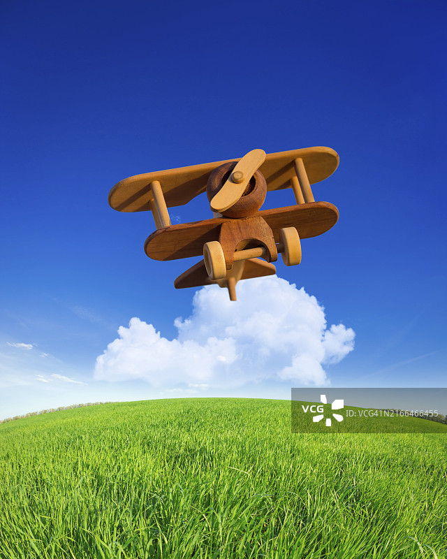 在夏季蓝色天空中飞行的木制玩具飞机：度假概念图片素材