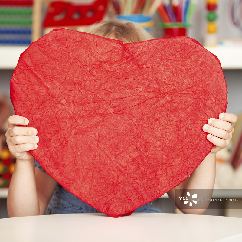 快乐的孩子在课堂上拿着手工制作的红色大纸心。情人节概念图片素材