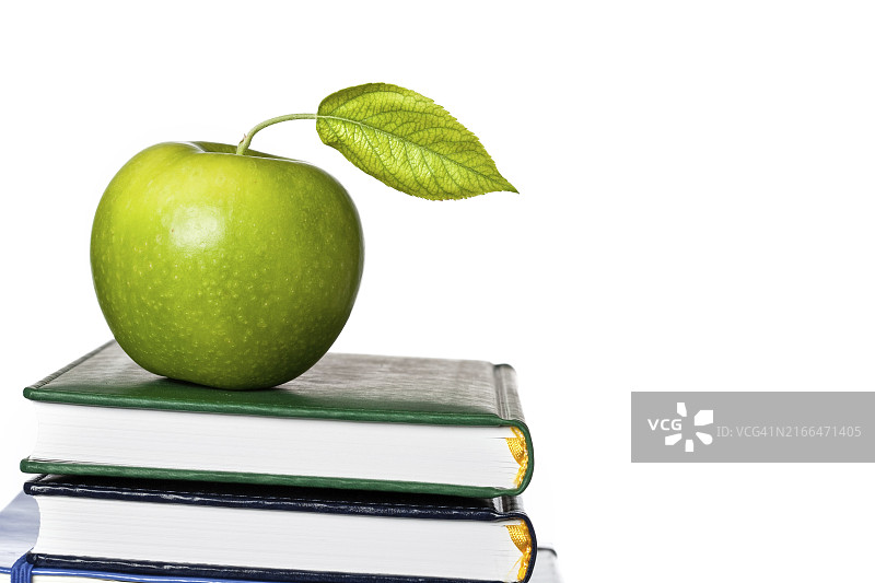 白色背景教科书上带有新鲜叶子的青苹果，学校概念图片素材