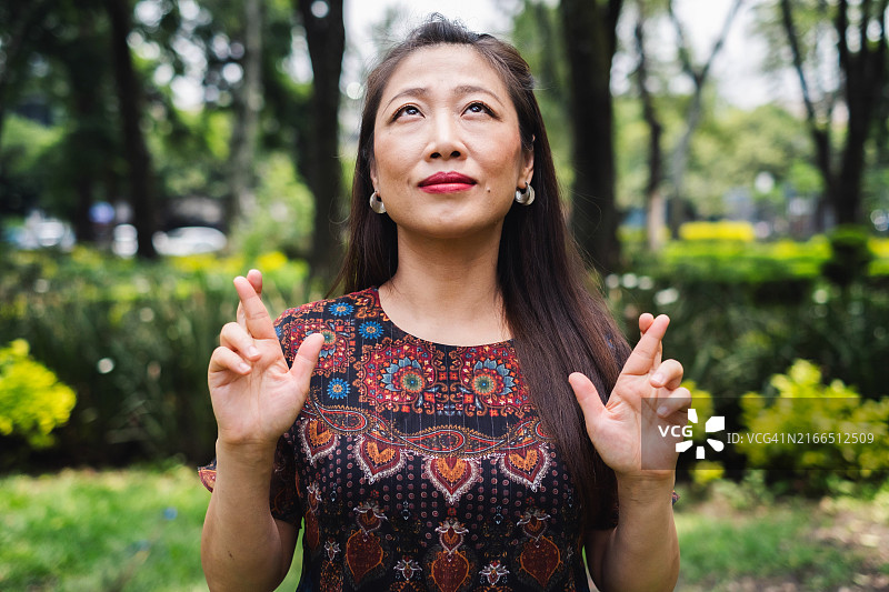亚洲女性抬头，交叉手指，满怀希望地许愿。图片素材
