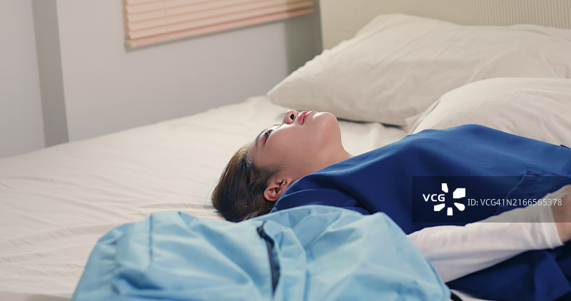 穿着工作服在床上休息的疲惫医护人员图片素材
