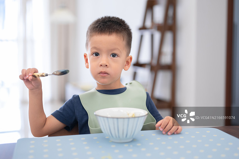男孩拿着勺子，一边吃东西一边看着镜头，可见白色背景图片素材