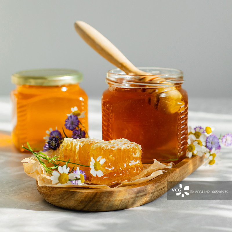 白色背景上的玻璃罐蜂蜜、蜂巢和木勺。有机生态产品。阳光阴影图片素材