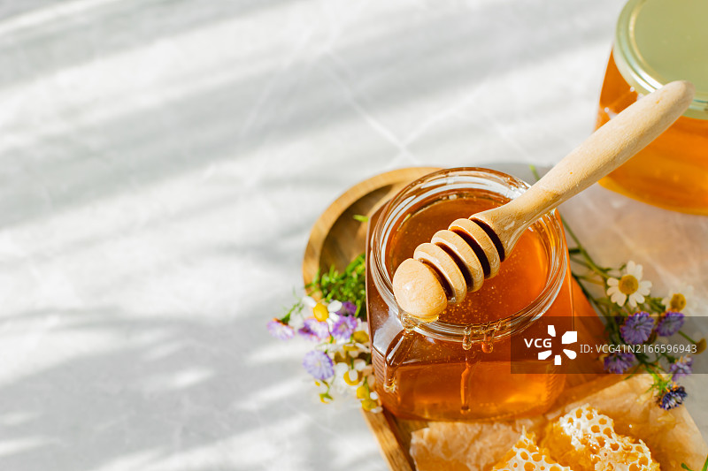 白色背景上的玻璃罐蜂蜜、蜂巢和木勺。有机生态产品。阳光阴影图片素材