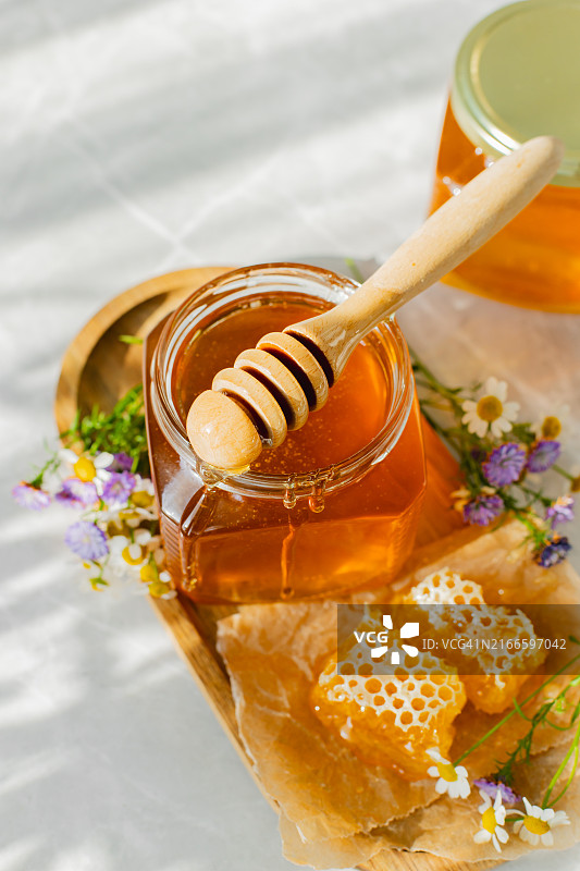 白色背景上的玻璃罐蜂蜜、蜂巢和木勺。有机生态产品。阳光阴影图片素材