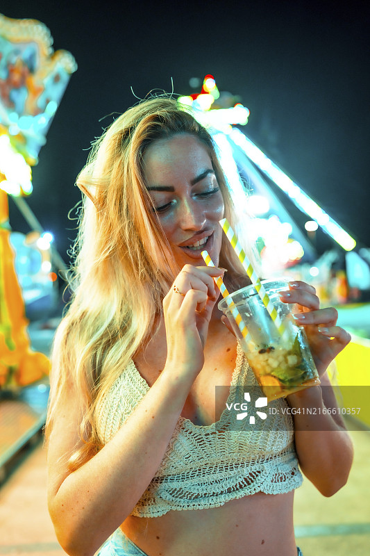 一个美丽的女人晚上在游乐园喝鸡尾酒的垂直特写肖像图片素材
