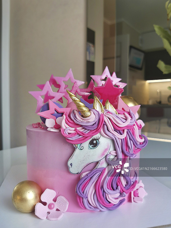 异想天开的独角兽生日蛋糕，粉色和金色装饰，以粉彩花朵和星星为点缀图片素材