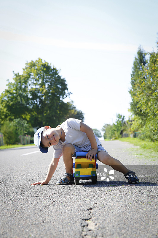 阳光明媚的日子，男孩在树木环绕的空旷道路上玩玩具卡车图片素材