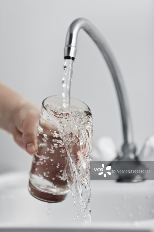 手持玻璃杯在厨房水龙头下接水图片素材