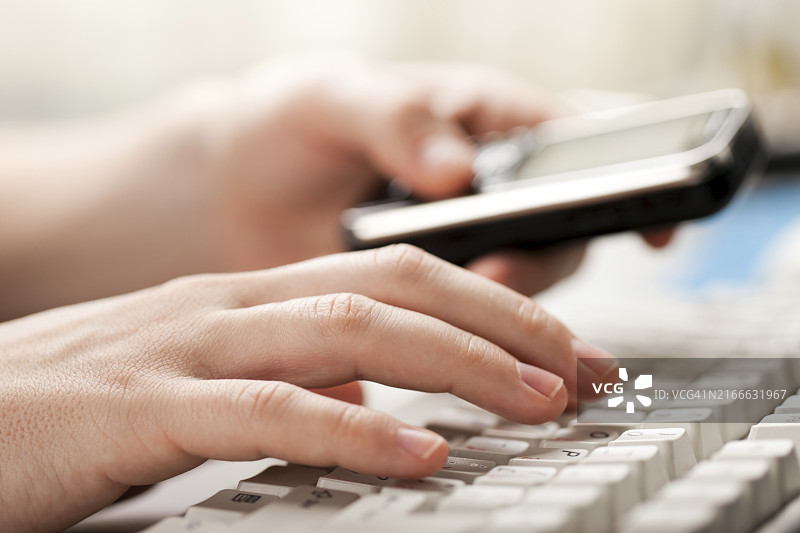 手持手机在电脑键盘上打字图片素材