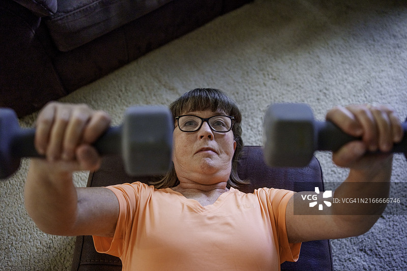 六旬女子在家用哑铃在矮榻上做卧推图片素材