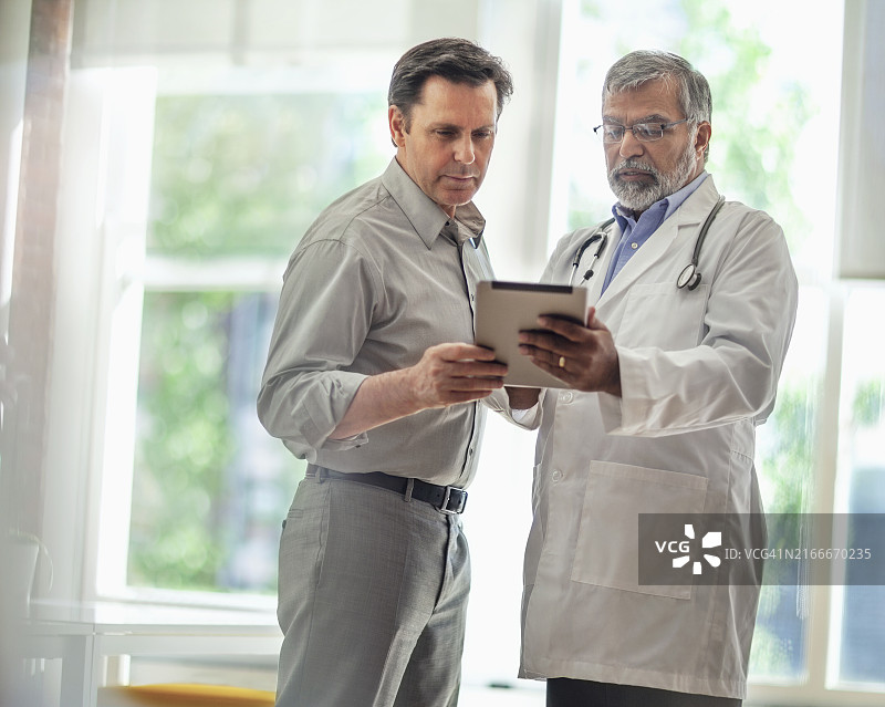 亚裔印度裔太平洋岛民男医生在诊所用平板电脑与中年男人交谈图片素材