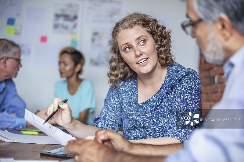 商务会议期间，中年妇女微笑地与办公室同事交谈图片素材