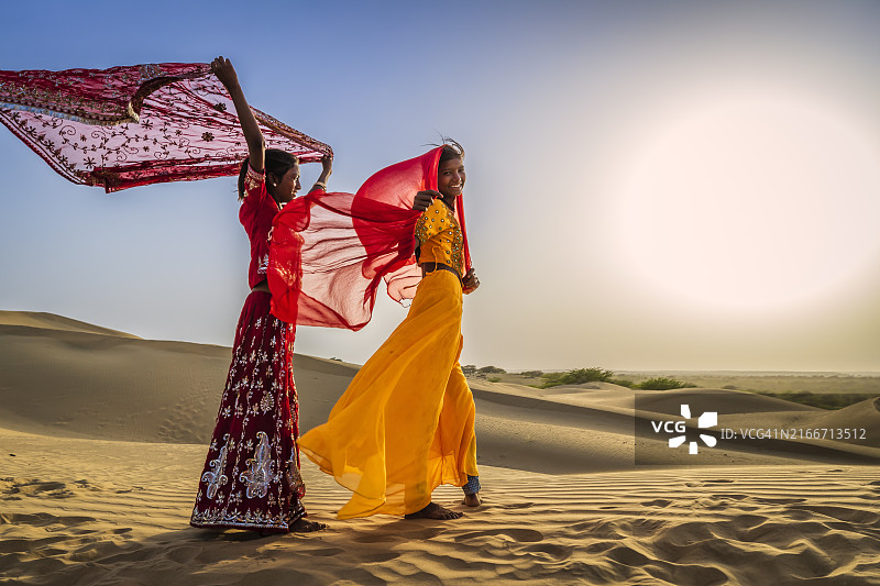 沙漠村庄沙丘上看日落的两位印度女孩图片素材