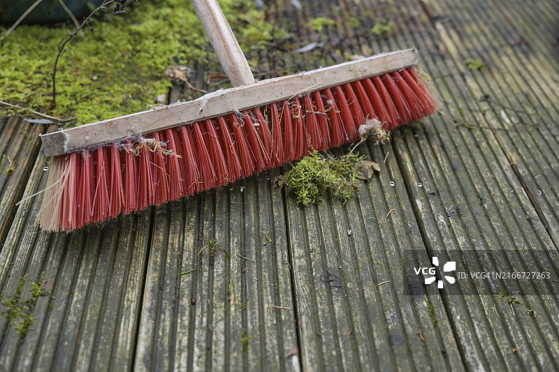 在布满藻类和苔藓的木甲板上，一把红色塑料刷毛的户外扫帚，花园和庭院春季清洁图片素材