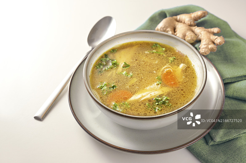 碗中盛有蔬菜、姜和欧芹的自制鸡汤，搭配绿色餐巾和勺子图片素材