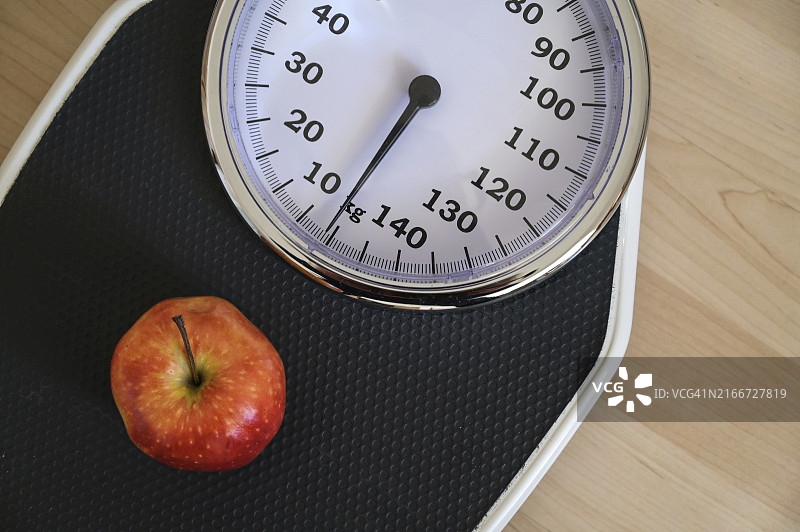 木地板上模拟个人体重秤上的红色苹果，健康饮食概念图片素材