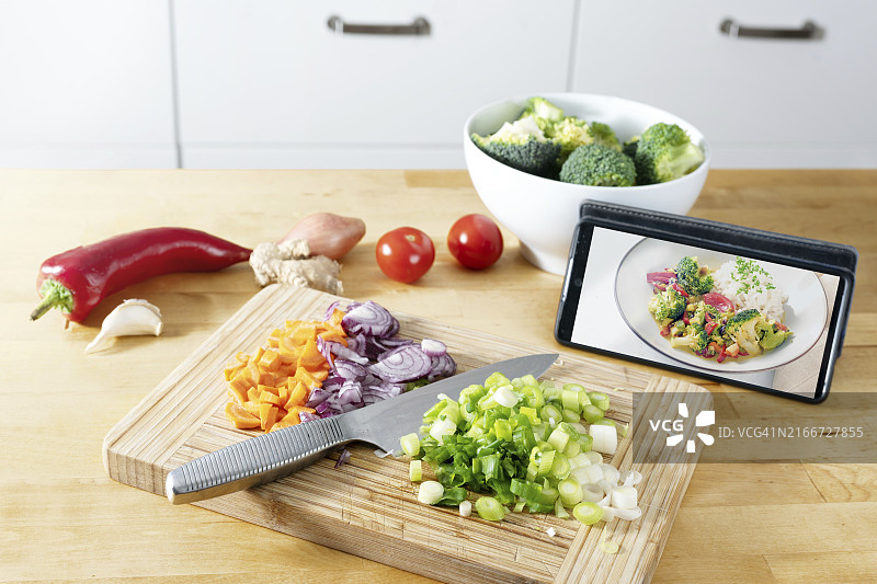 在木制案板上切蔬菜，用手机查看食谱，使用APP烹饪健康膳食图片素材