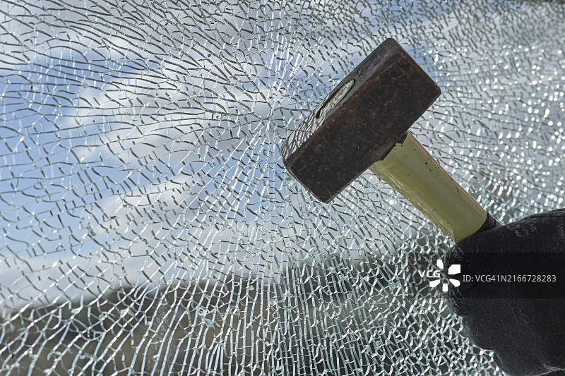 罪犯戴着手套用锤子破坏玻璃，暴力盗窃概念图片素材
