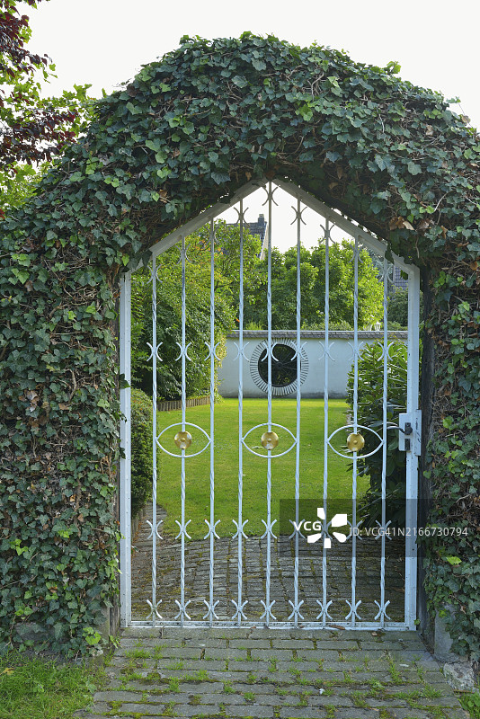 覆盖常春藤的拱门和白色铁艺花园通往宁静的草坪，德国图片素材