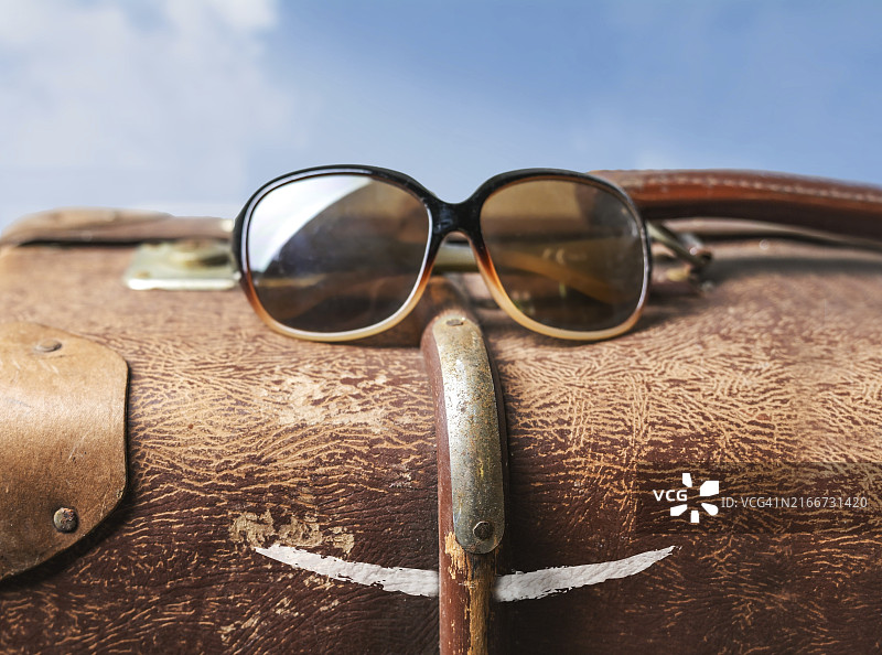 戴着太阳镜和画着嘴巴的旧棕色手提箱的有趣旅行面孔图片素材