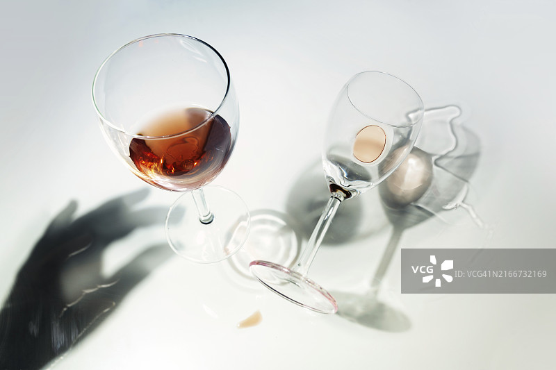 红酒杯，以不寻常的视角站立和倒下，在明亮背景上手的倒影和阴影，派对或酒精成瘾概念的抽象痕迹图片素材