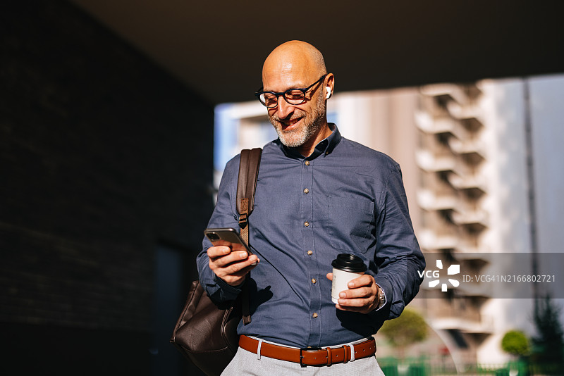 在城市里边走边喝咖啡玩手机的商人图片素材