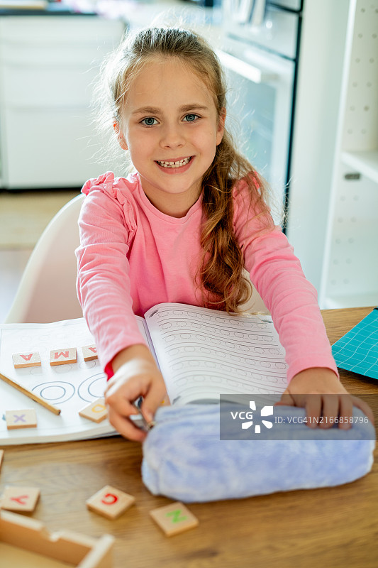 6岁的可爱小女孩在厨房的桌子上做作业。回到学校。图片素材