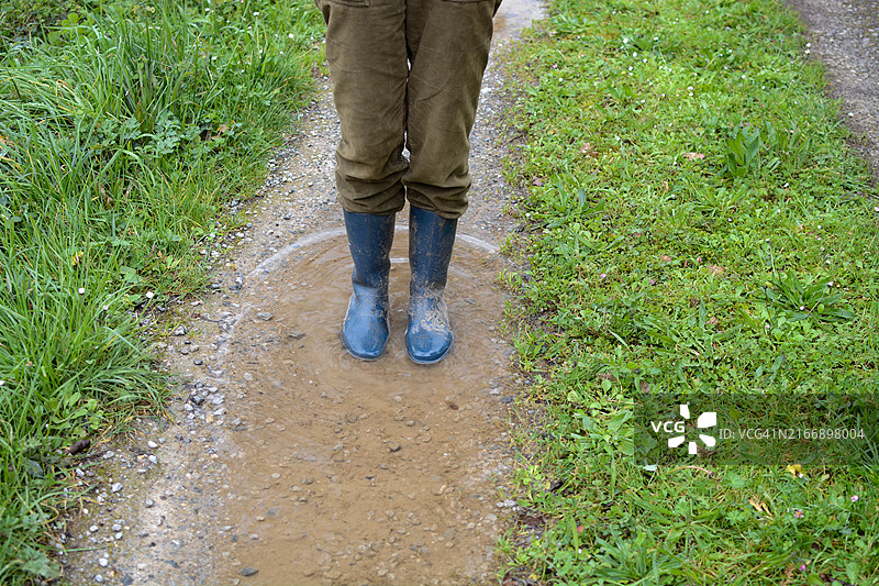 乡村小路上水坑中蓝色雨靴的低角度视角图片素材