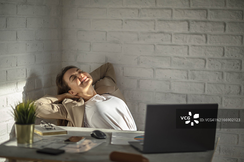 坐在桌旁伸展背部、手臂的微笑年轻白人女经理图片素材