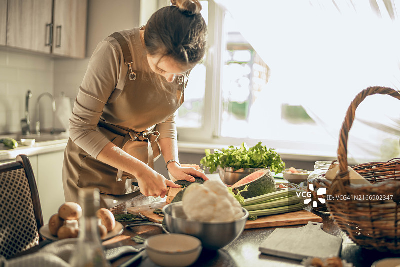 年轻女人削绿色南瓜，烹饪纯素午餐图片素材