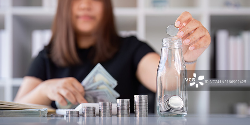 女人将硬币放入玻璃罐中存钱图片素材
