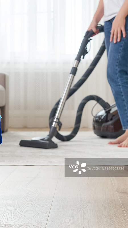 女人用真空吸尘器清洁客厅地毯图片素材