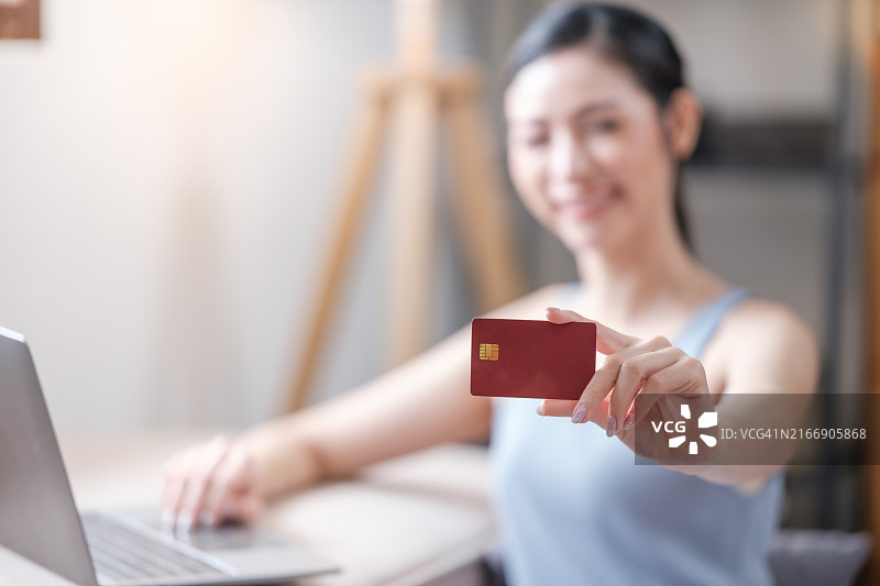 年轻亚洲女人在家使用信用卡在电脑上进行网上购物图片素材