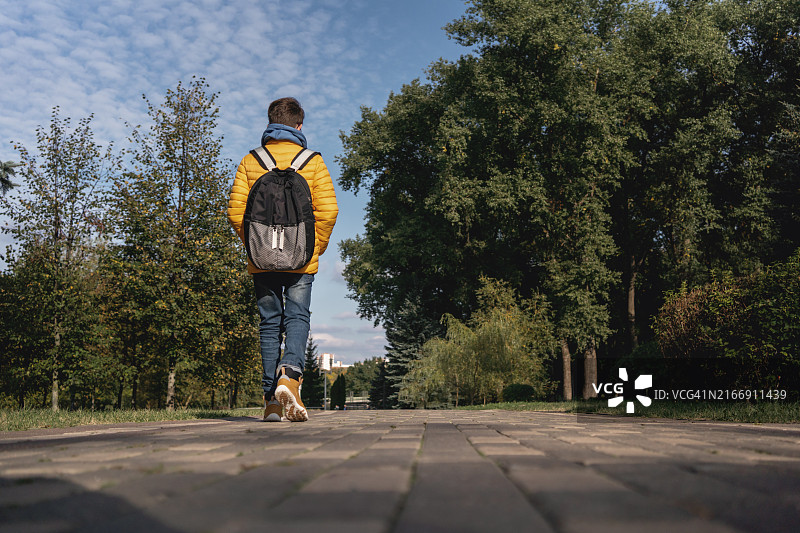 穿黄色夹克的青少年男孩在公园里背对镜头走开图片素材