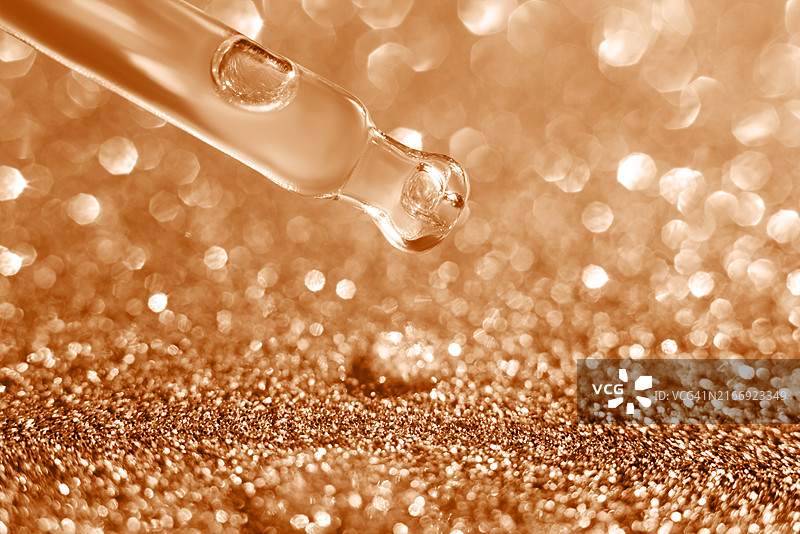 化妆品玻璃滴管移液器，末端有一小滴透明质酸天然精华液，位于粉色闪光背景上。图片素材