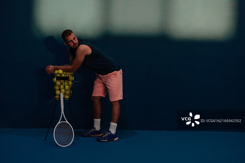 休息在装满网球的篮子上的男子网球运动员图片素材