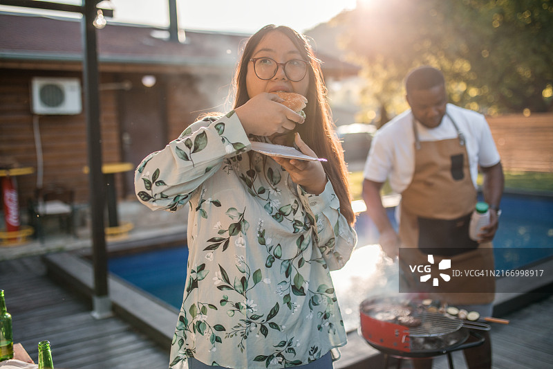 亚洲女人在游泳池边享用汉堡图片素材
