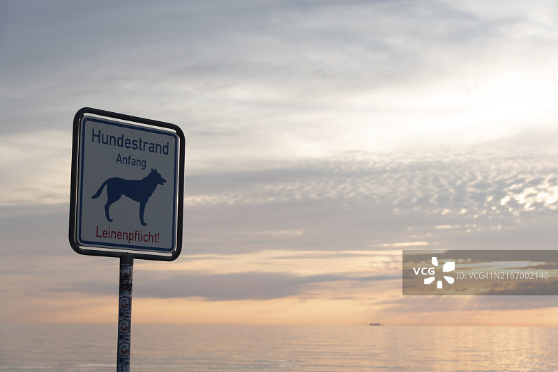 波罗的海菲施兰-达尔斯-青斯特半岛狗海滩日落标志,附平静海面和多云天空,狗标志和牵引绳要求通知,德国梅克伦堡-前波美拉尼亚州迪尔哈根图片素材