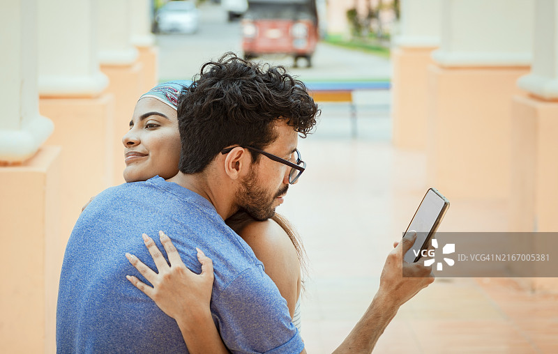 拥抱女友时看手机的男人图片素材