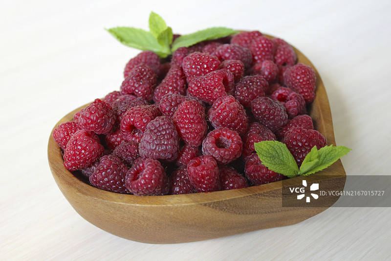 盛满新鲜覆盆子并用薄荷叶装饰的心形木碗图片素材