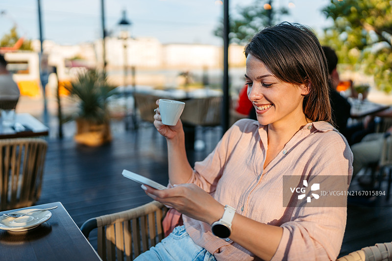 在匈牙利布达佩斯街边咖啡馆用手机喝咖啡的年轻女人图片素材