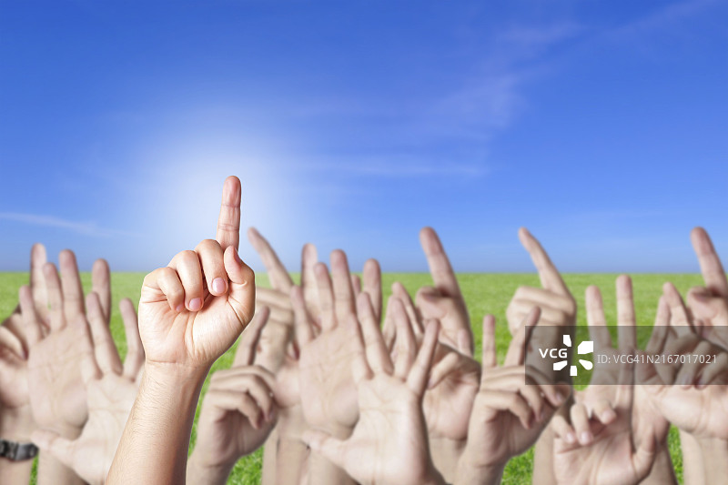 一群人在绿地上举手回答问题，蓝天图片素材