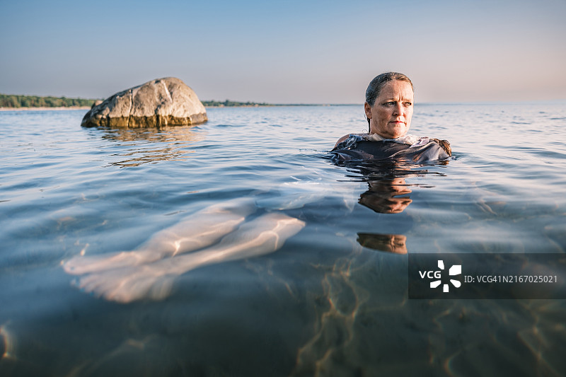 在海滩日落时分漂浮在水中的中年妇女图片素材