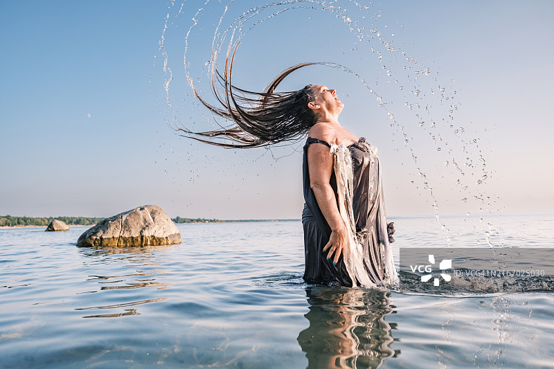 夕阳下在海滩甩长发的中年妇女图片素材