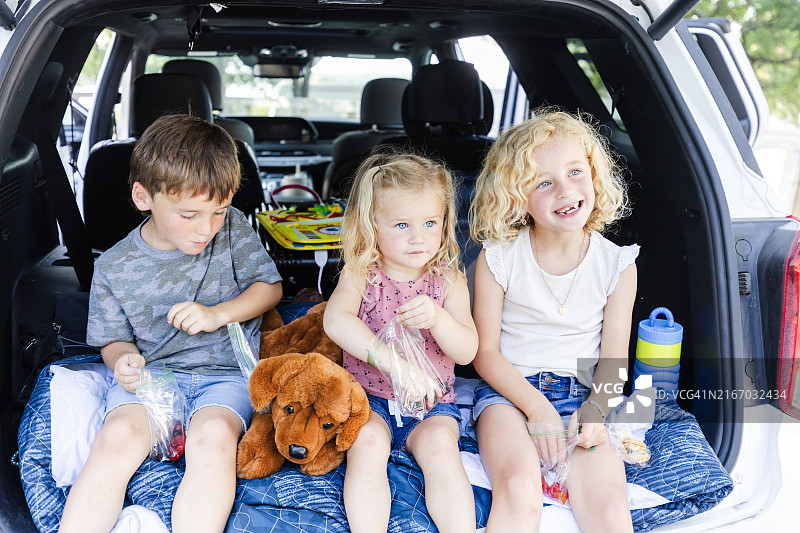 年轻的兄弟姐妹坐在汽车后座享用零食图片素材