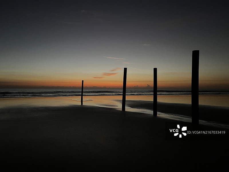 海滩上，木桩在橙色天空的映衬下呈现剪影图片素材