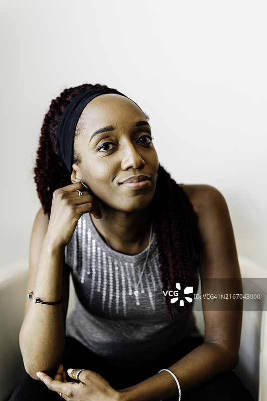 迷人的年轻非裔美国女子留着长发，坐在室内看着镜头，拍摄一张非正式肖像图片素材
