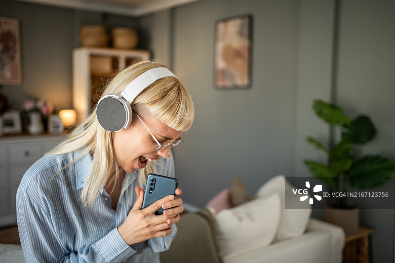 年轻女人戴着无线耳机在客厅享受音乐图片素材