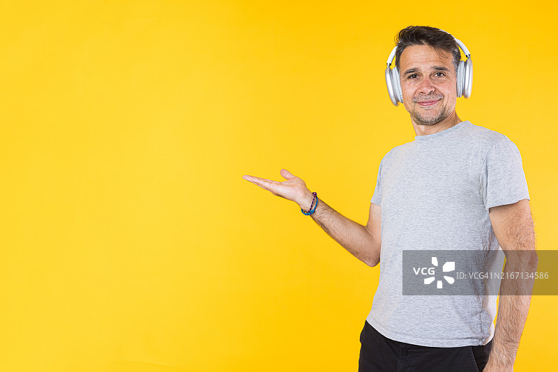 微笑男人戴降噪耳机听音乐，黄色背景图片素材
